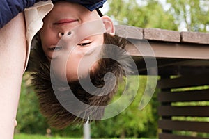 Eight-year-old boy hangs upside down from a bench at his mother`s legs. Funny picture about of children`s pranks photo