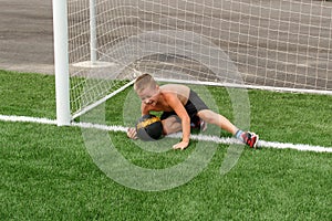 An eight-year-old Caucasian boy in black shorts catches a soccer ball in the goal in the summer
