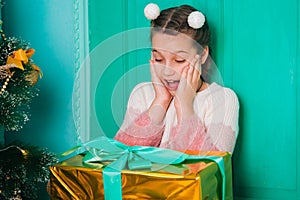An eight-year-old girl in a pink sweater sits on the steps by the Christmas door holding a joyful present
