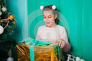 An eight-year-old girl in a pink sweater sits on the steps by the Christmas door holding a joyful present