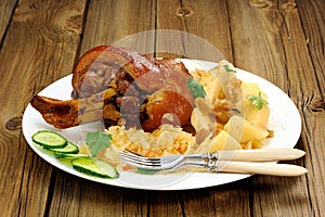 Eisbein in white plate with two forks on wooden background