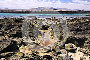 El Cotillo, North Fuerteventura: View over bright scattered stoneson beach in shallow water on turquoise lagoon of beach La Concha