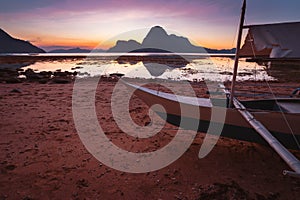 El Nido bay with local banca boat on shore on sunset at low tide. Picturesque nature scenery. Palawan, Philippines