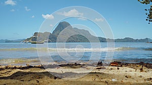 El Nido bay. Palawan, Philippines. Banca boat in sunny summer lagoon. Calm waves rolling on sandy beach coastline