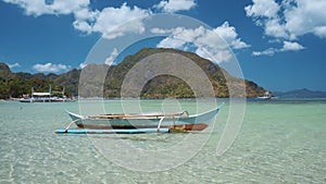 El Nido bay. Palawan, Philippines. Bangka boat floating in shallow bay with village and mountain in background