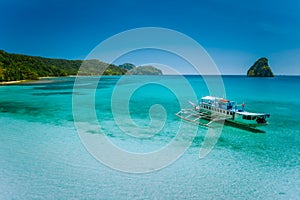 El Nido island hopping trip. Boat moored in calm blue shallow turquoise ocean lagoon with secluded rocky shark fin shape photo