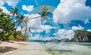 El Nido, Palawan, Philippines. Exotic beach with palm trees, tourist boat on the sandy beach and blue sky with white