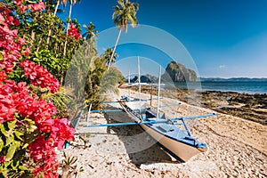 El Nido, Palawan, Philippines. Native banca boat and vibrant flowers at Las cabanas beach with amazing Pinagbuyutan