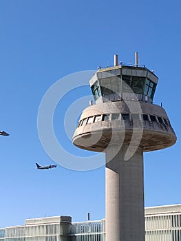 El Prat Barcelona airport control tower, with a plane taking off flying next to it.