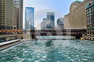 El train travels over a blue and frozen Chicago River with ice chunks.