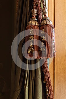 Elaborate large window curtain tie back tassels, cords, and trim over green silk curtains, warm wood background