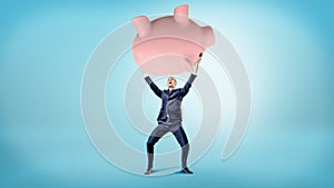 An elated businessman holds up a giant overturned piggy bank over his head.