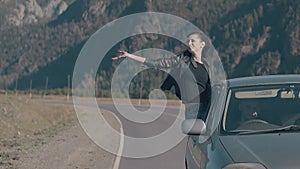 Elated lady sits on blue speeding car and raises hand to sky