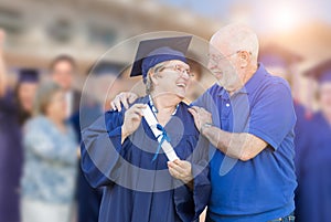 Elated Senior Adult Woman In Cap and Gown Being Congratulated By Husban
