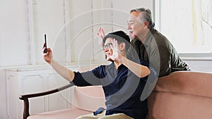 Elder Asian man and his son using video call from mobile phone to say hi to the rest of his family in his retirement home