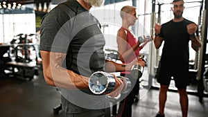 Elder bodybuilder with heavy dumbbells in sport center