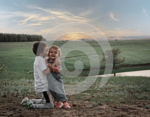 The elder brother kisses his little sister against the backdrop of a picturesque landscape