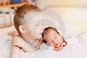 Elder brother and newborn baby sister lying on bed at home