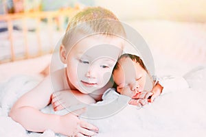 Elder brother and newborn baby sister lying on bed at home