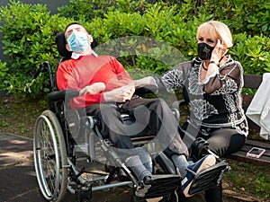 Elder Caucasian woman holding the hand of her husband while sitting in a wheelchair