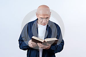 Elder hairless man wearing eyeglasses holding and reading book