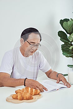 Elder man drinking milk and reading book while having breakfast