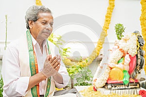 Elder man offering Bhajan or hymn in front of Lord Ganesha Idol during Ganesha or vinayaka Chaturthi festvial ceremony