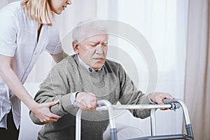 Elder man with walker and young nurse supporting him photo