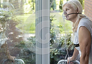 Elder person with an oxygen breathing mask looking at a window