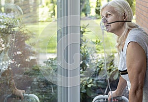 Elder person with an oxygen breathing mask looking at a window photo