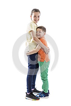 Elder sister teenager with younger brother 6-7 years old laugh and hug. Children in bright yellow-orange and green clothes. Love