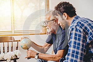 Elder uncle telling world adventure story in the pass to his son hand pointing at distination country in world map model at home