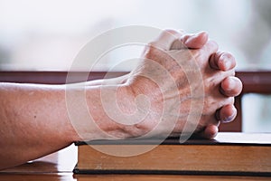 Elder woman hands folded in prayer on a Holy Bible