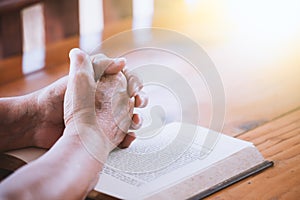 Elder woman hands folded in prayer on a Holy Bible