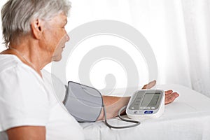 Elder woman measuring blood pressure with automatic manometer at