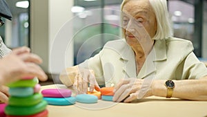 Elder woman playing skill games with round pieces in geriatrics