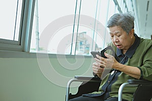 elder woman in wheelchair holding mobile phone surprised shocked
