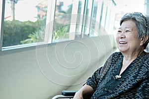 elder woman on wheelchair smiling & resting near window. happy e