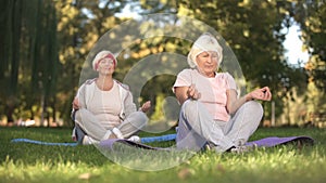 Elder women sitting in lotus position and meditating doing yoga in park, energy