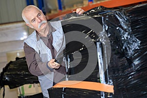 elder worker using shrink wrap to pack items in warehouse