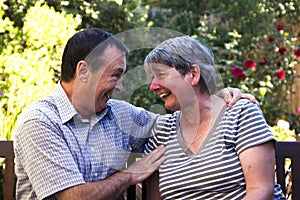Elderley couple sitting on a bench laughing