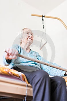 Elderly 96 years old woman exercising with a stick sitting on her bad.