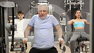 Elderly active man exercising on a simulator in a modern gym