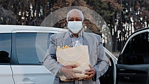 Elderly african american man in protective medical mask in street parking bought groceries in fruit shop senior male