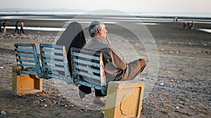 Elderly Arabian couple sit on a bench and look at the sea