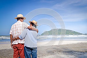 An elderly Asian couple hugging each other on the beach.