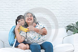 elderly Asian grandmother and her granddaughter is 6-year-old sitting on white sofa, are hugging, smile and happy together