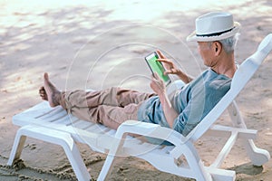 An elderly Asian man happily lounging on his laptop on a relaxing day at the beach