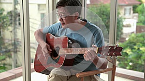 Elderly Asian man resting playing guitar in the living room.