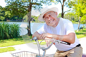 Elderly Asian man sitting on a bicycle in an outdoor park.